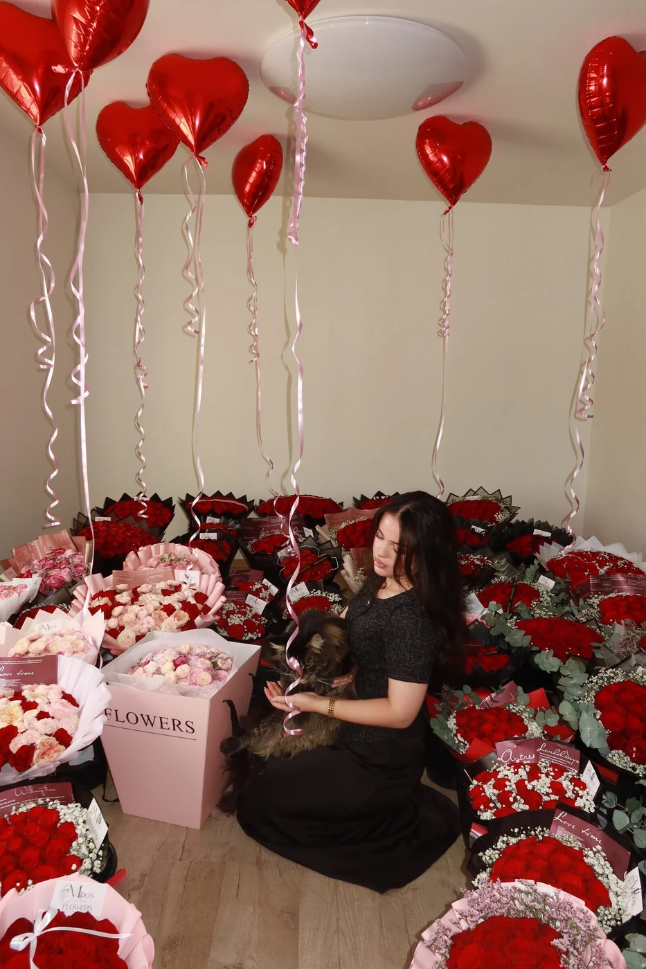 Florist från Midosflowers omgiven av röda rosbuketter, blomsterboxar och hjärtballonger inför Alla hjärtans dag